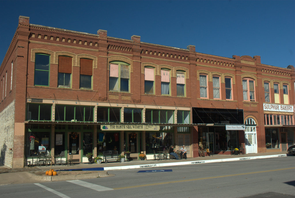 A two-story downtown brick building. People are sitting at a table in front of a business.