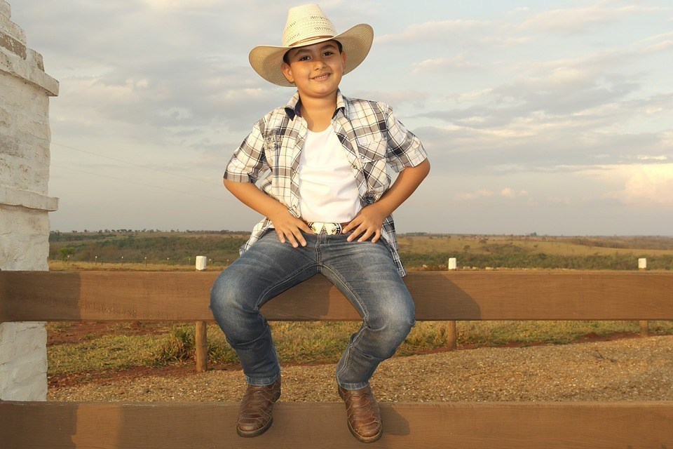 A young Latino cowboy smiles while sitting on a board fence